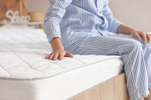 A boy in pyjamas sitting on a comfortable mattress in the morning