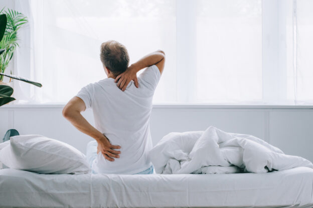 Man sitting on a bed and experiencing morning back pain